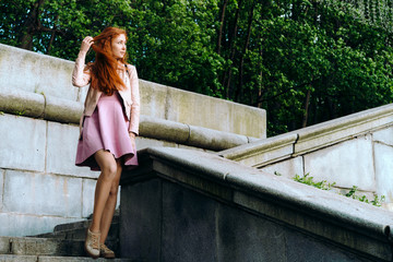 Naklejka premium Red-haired girl in pink on the steps
