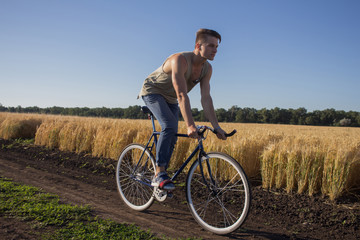 Young man ride fixed gear bike on the country road, fields and blue sky background 