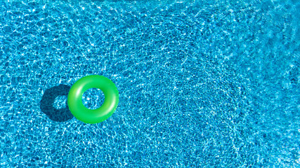 Aerial view of colorful inflatable ring donut toy in swimming pool water from above, family vacation concept background
