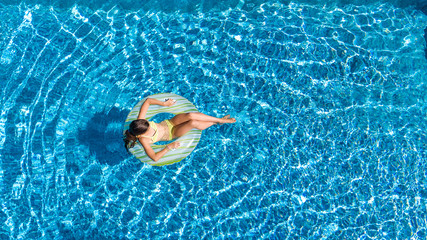 Aerial view of girl in swimming pool from above, kid swim on inflatable ring donut and has fun in water on family vacation
