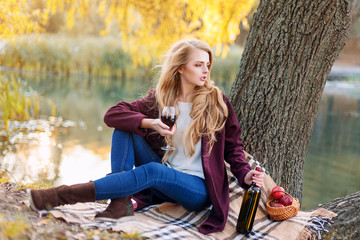 Beautiful woman drinking wine outdoors having picnic in the park. Portrait of young blonde beauty...