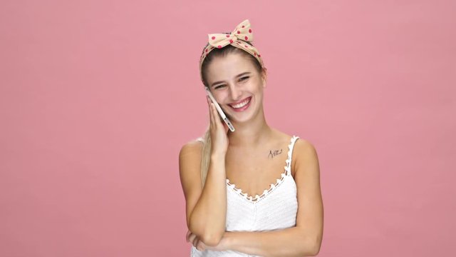Young sad caucasian woman talking with friends by phone over pink background