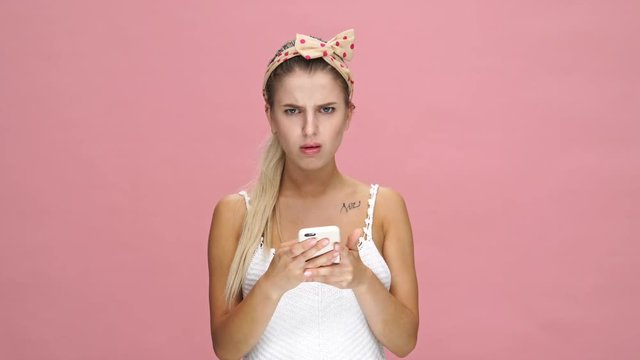 Young angry caucasian woman chatting by phone over pink background