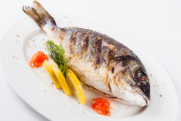 grilled dorada on a white plate on a light background (close)