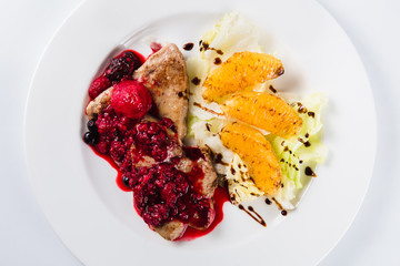 Foie gras in a sauce of wild berries with a lettuce leaf and orange on a white plate on a light background (top view close)