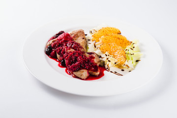 Foie gras in a sauce of wild berries with a lettuce leaf and orange on a white plate on a light background (close)