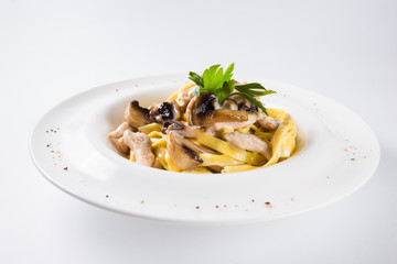 Pasta with chicken and mushrooms on a round white plate on a light background (close)