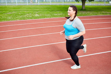 Obraz premium Overweight young woman in activewear trying to get fit and running on stadium