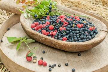 Forest raspberries and blueberries in a wooden old container. Old simple rough farming subjects. Vintage style.
