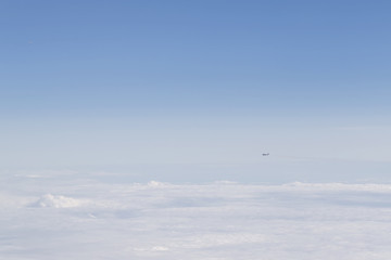 View of an airplane flying from the window of another airplane flying above the clouds