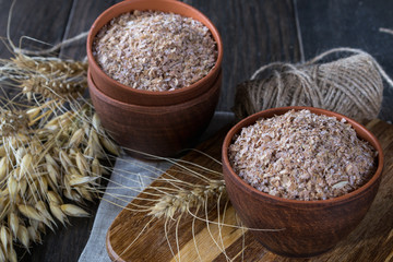 Wheat, Oat bran in clay  bowl and ears of wheat and oat.  Dietary supplement to improve digestion. Ondark wooden background