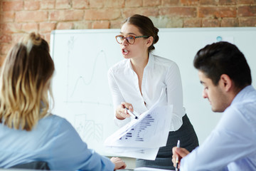 Confident economist pointing at financial document and voicing her opinion to colleagues