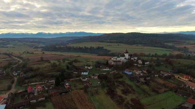 Aerial drone slow shot over Hosman, a saxon village from Transylvania, Romania.	Autumn countryside view in foreground and Fagaras Mountains in background. 4k footage. 