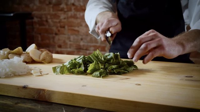 Cookery lessons. The chef cutting green leaves of basil up on a wood chopping board in the kitchen of a restaurant. 4K