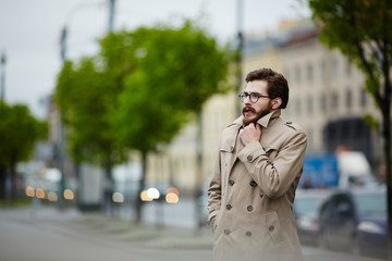 Young man in trenchcoat waiting for taxi in rainy weather