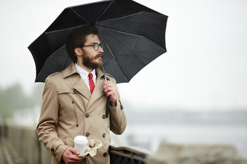 Elegant man with black umbrella and drink having walk in the city