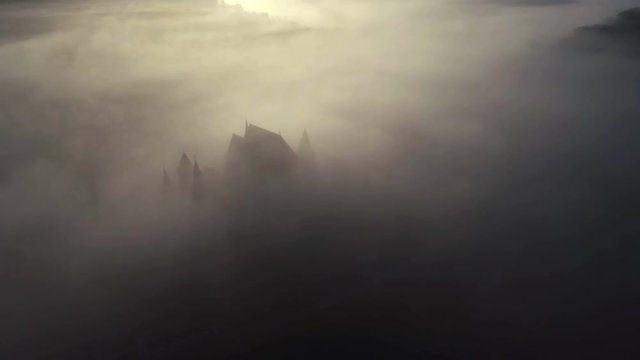 Aerial drone slow shot over medieval church in remote village. 4k footage. Transylvania, Romania.	Autumn fog creating idyllic atmosphere with the old church appearing through clouds.