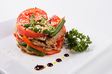 meat salad, tomato decoration on a white plate on a light background