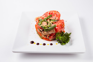 meat salad, tomato decoration on a white plate on a light background