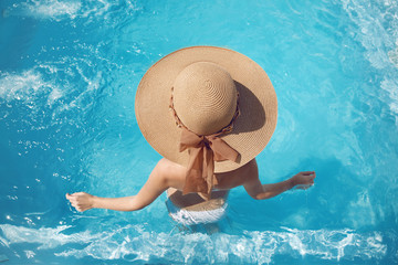 Back view of woman in straw hat relaxing in swimming pool on Tropical Resort. Exotic Paradise. Travel, Tourism and Vacations Concept.
