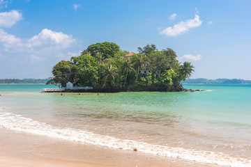 The white sandy beach and bay of Weligama with Taprobane Island in the foreground. Originally called Galduwa in Sinhalese, it means rock island. The beach in the south is very popular with surfers.	