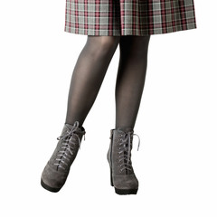 Female legs in gray pantyhose, a skirt in a cage and in gray suede boots on a heel on an isolated...
