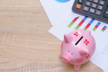 Pink piggy bank with graph and calculator on wooden desk - growing interest rate concept.