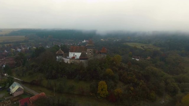 4k aerial orbit flight around medieval church in Viscri, a saxon village from Transylvania, Romania.	Countryside view with Viscri fortified church in the middle surrounded by saxon houses.