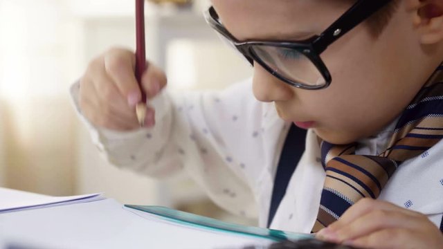Small child boy in white shirt and tie images he is smart businessman working with papers and calculator, making notes, like adult professional, dreaming to be as his father, sitting at the table