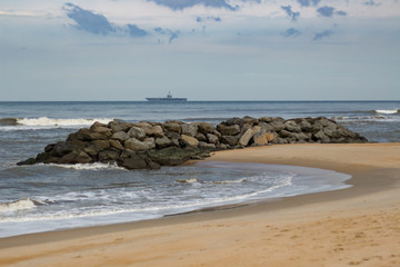 Cargo ship on the horizon, beach and breakwater in foreground