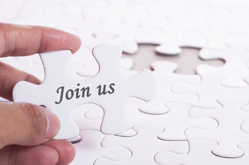 Hand holding a piece of jigsaw puzzle with a word Join Us. Financial Concept.