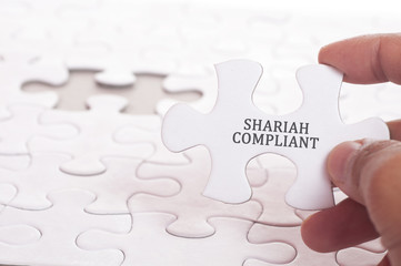 Hand holding a piece of jigsaw puzzle with a word Shariah compliant. Financial Concept.