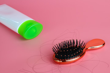 Hairbrush or Comb with some hair on its showing the hair fall problem and conditioner tube on pink background. 