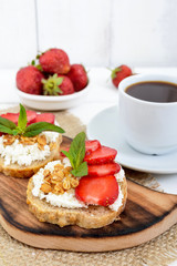 Delicious healthy dietary breakfast: rye bread with cottage cheese and strawberries and a cup of coffee (espresso) on a white wooden background.