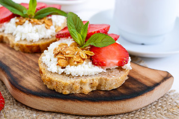 Delicious healthy dietary breakfast: rye bread with cottage cheese and strawberries  on a white wooden background.