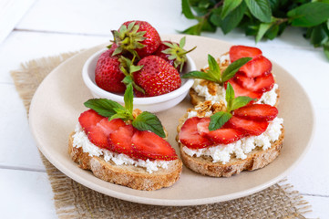 Delicious healthy dietary breakfast: rye bread with cottage cheese and strawberries  on a white wooden background.