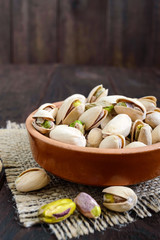 Useful nuts - pistachios in a ceramic bowl on a dark wooden background. Vertical view