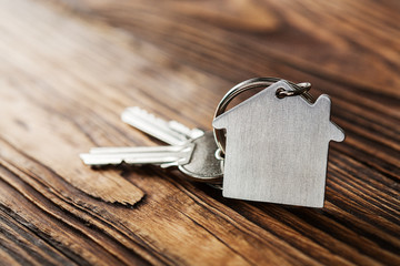 Symbol of house with silver key on wooden background