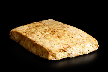 Single block of marinated tofu isolated on black.