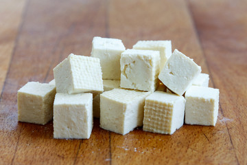 Cubes of cut white tofu on wooden chopping board.