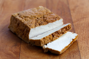 Block of smoked tofu and two tofu slices on wooden chopping board.
