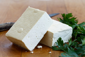 Two blocks of white tofu with fresh parsley and rustic knife on wooden chopping board.