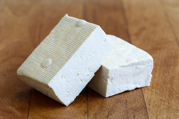 Two blocks of white tofu on wooden chopping board.