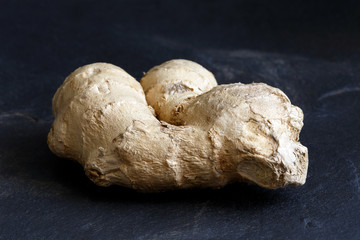 Whole ginger root isolated on black slate.