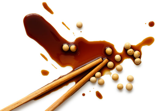 Spilled Soya Sauce And Soya Beans On White From Above With Chopsticks.