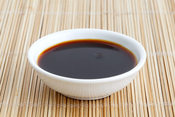 Soya sauce in white ceramic bowl isolated on bamboo mat.