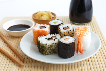 Selection of sushi on bamboo mat with chopsticks, soya sauce and pickled ginger.