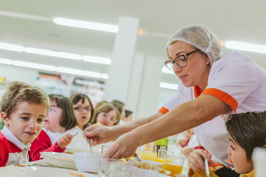 Woman Instructor Caring a Group of Children during the Meal at the School Canteen