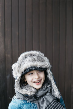 Portrait of a boy in front of wooden background wearing a furry hat,looking away