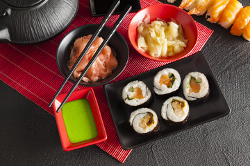 Sushi set and black teapot on red mat and black table